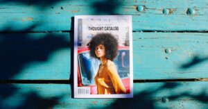 Thought Catalog magazine lies on a textured wooden surface, showcasing a stylish cover with vibrant shadows.